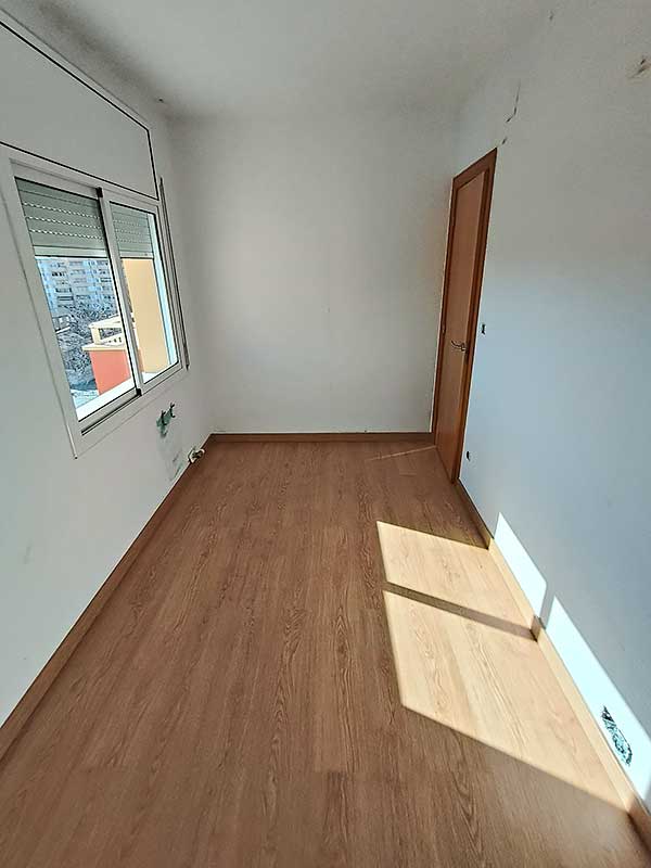 GS-Serveis colocación suelo de parquet Una habitación con suelo de madera y una ventana que permite la entrada de luz natural.