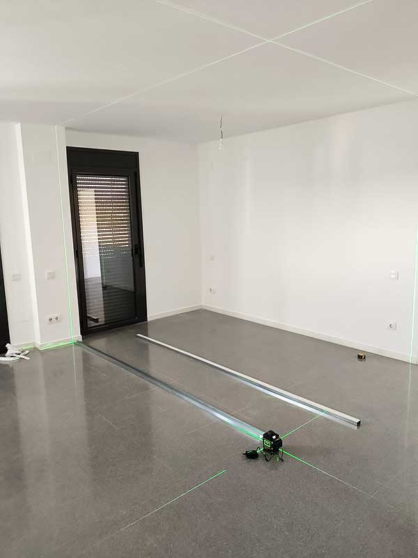 Trabajo instalación pladur GS Serveis Espacio interior con una línea láser verde en el suelo.