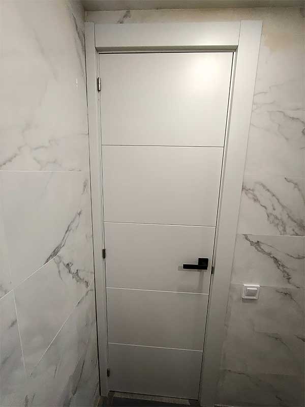 Montaje puertas interior Gs-Serveis Puerta blanca en un baño con paredes de mármol.