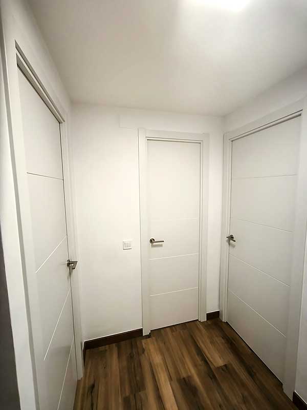 GS-Serveis montaje de tres puertas Espacio interior con tres puertas blancas y un suelo de madera.