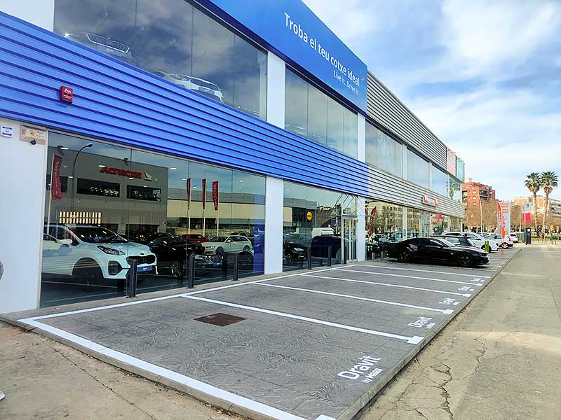 Gs-Serveis Trabajo de pintura Concesionario Concesionario de automóviles con un edificio azul y blanco, exhibiendo una variedad de vehículos.