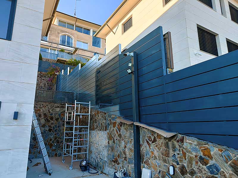 GS-Serveis Trabajo de pintura vaya de vivienda Cerca azul sobre pared de piedra, con una escalera apoyada sobre ella.